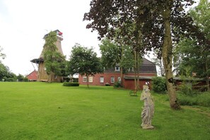 A grassy area with a statue, a red brick building, and a tower with a red roof.