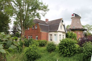 A traditional brick house with a thatched tower, surrounded by lush greenery.