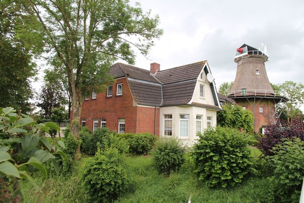 A traditional brick house with a thatched tower, surrounded by lush greenery.
