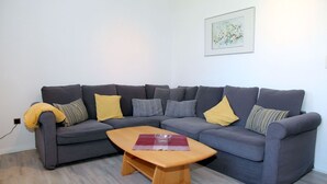 Een moderne woonkamer met een grijze hoekbank, een houten salontafel en een gekaderd kunstwerk aan de muur.