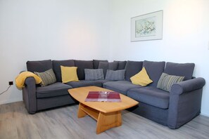 A modern living room with a grey sectional sofa, a wooden coffee table, and a framed artwork on the wall.