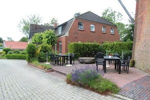 Ein Backsteinhaus mit Garten und einer Terrasse, die Sitzgelegenheiten und eine Feuerstelle bietet.
