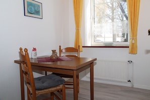 Un comedor con una mesa de madera, dos sillas, un jarrón y un cuadro en la pared.