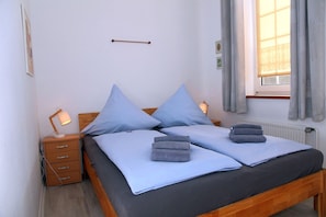 Una cama doble con dos almohadas, una mesita de noche con lámpara y una ventana con cortinas.