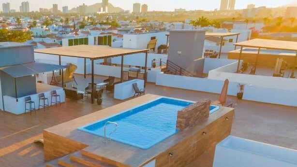 Una piscina en la azotea con cubierta de madera y escalones de acceso, rodeada de mobiliario exterior y vistas a la ciudad.