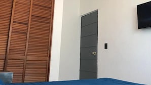 Un dormitorio con una cama, un armario de madera, una puerta gris y un televisor montado en la pared.