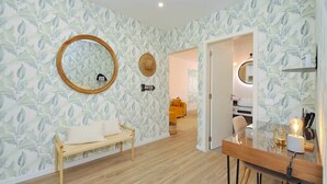 A modern living room with a wooden bench, a round mirror, and a wall with a leafy pattern. - Tropical Pool View Cascais - Checkinhome (Cascais)