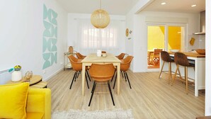 A modern dining area with a wooden table and chairs, a hanging light fixture, and a yellow accent wall. - Tropical Pool View Cascais - Checkinhome (Cascais)