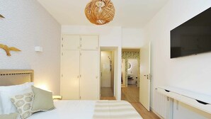 A bedroom with a bed, a wardrobe, a television, and a bathroom visible through an open door. - Tropical Pool View Cascais - Checkinhome (Cascais)