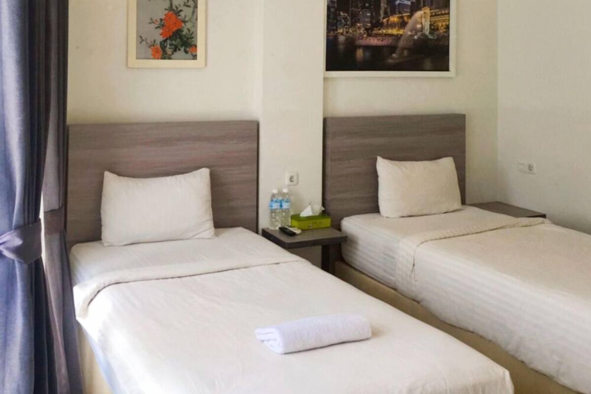 A hotel room with two single beds, a nightstand with a remote control, a water bottle, and a tissue box.