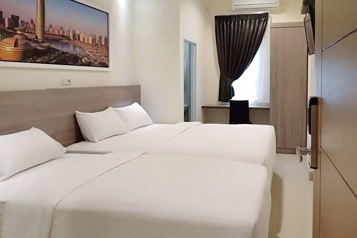 A hotel room with two beds, a cityscape painting, a window with curtains, and a wardrobe.