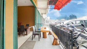 An outdoor seating area with a wooden bench and chairs, a table, and a railing. - TwoSpaces Living at Maximus Inn (Palembang)