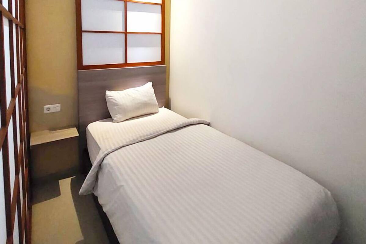 A small, neatly made bed with a headboard, a bedside table, and a window with frosted glass panels.