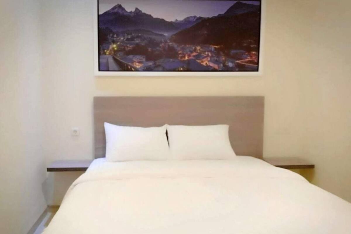A neatly made bed in a hotel room with a mountain landscape painting above it.