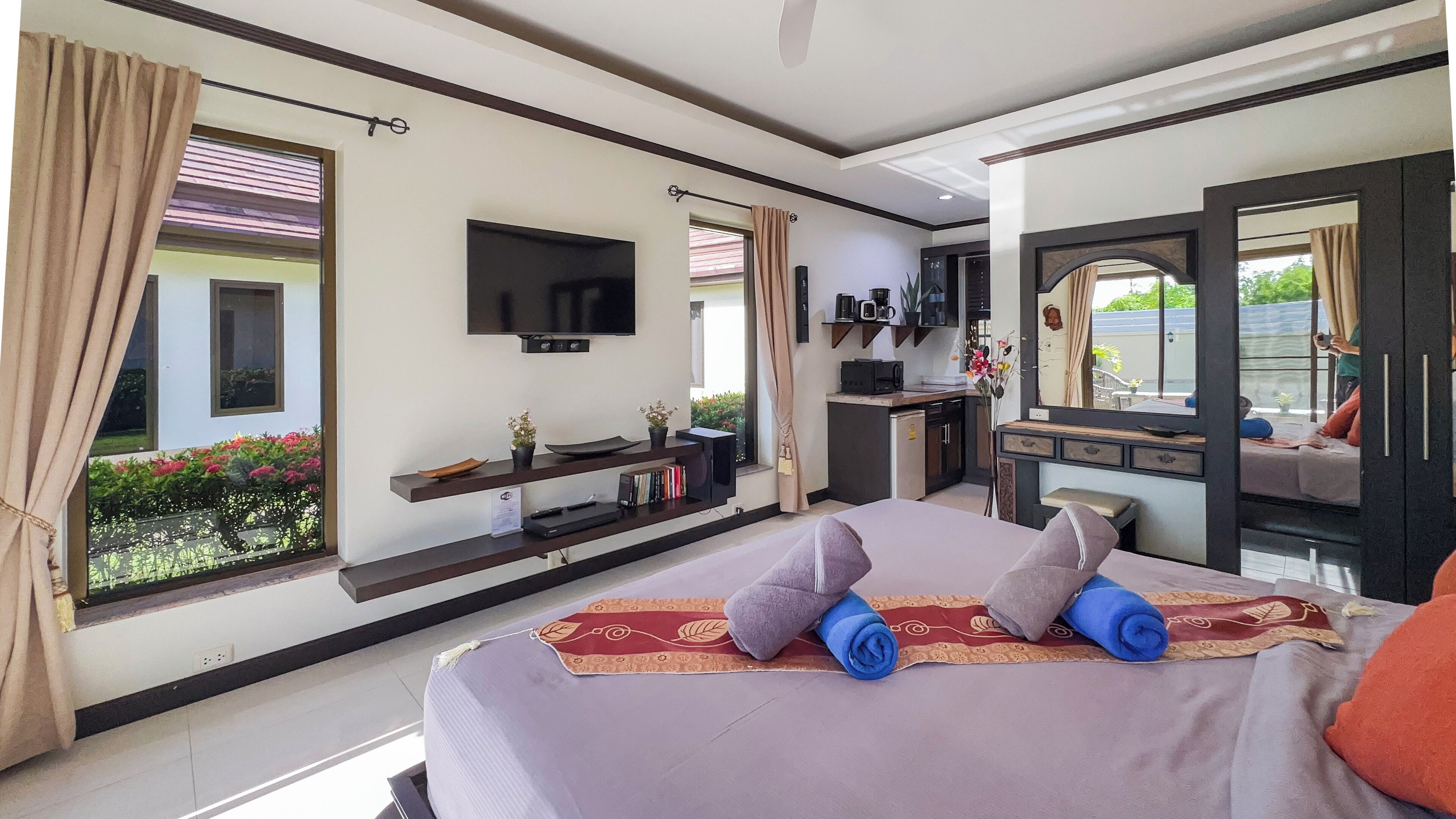 Une chambre d’hôtel avec un grand lit, un t éléviseur fixé au mur, une petite kitchenette et une fenêtre avec des rideaux.