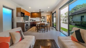 A modern apartment with a kitchen, dining area, and a large sliding glass door to a garden. - Garden bungalows 4br with private pool (Rawai)