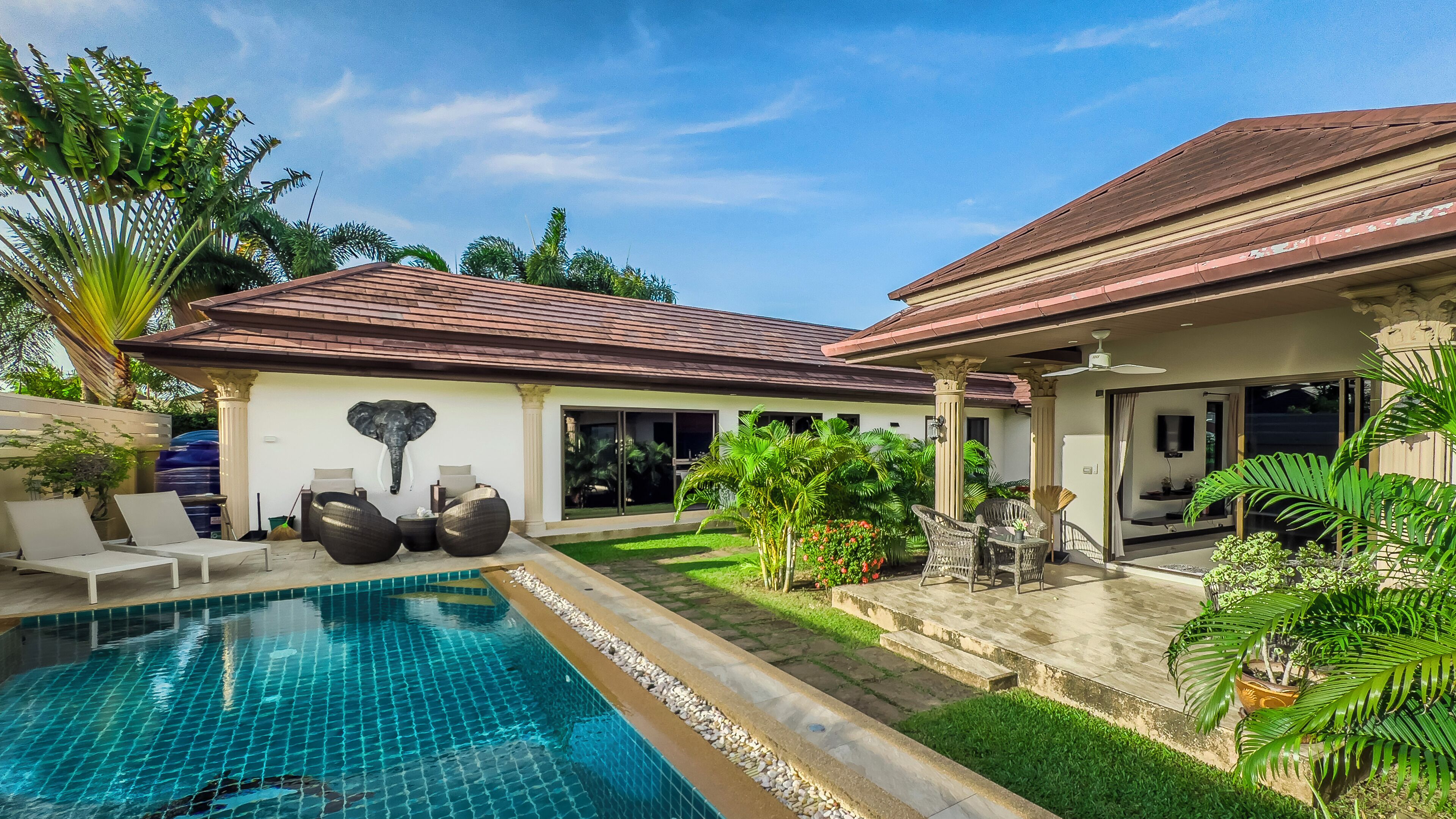 A poolside area with a swimming pool, lounge chairs, and a decorative elephant sculpture.
