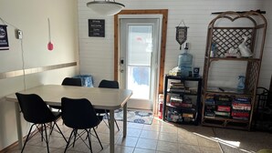 Un espace repas comprenant une table et des chaises, un distributeur d’eau et une étagère avec des jeux de société.