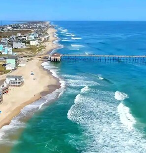 A coastal area with a beach, ocean waves, and a pier extending into the water. - Steps from the ocean in the Outer Banks - New Hot Tub, Deck & Dog Run! (Rodanthe)