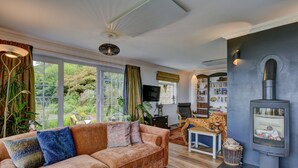 A living room with a sofa, a fireplace, a bookshelf, and large windows. - Gapperies, West Porlock (Porlock Weir)