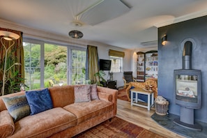 Una sala de estar con sofá, chimenea, estantería y ventanas amplias.