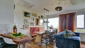 A dining area with a wooden table, chairs, and a blue sofa. There are framed pictures on the wall and a window with curtains. - Gapperies, West Porlock (Porlock Weir)