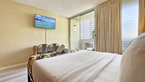 Ein Hotelzimmer mit Bett, Wandfernseher, Stuhl und Meerblick durch ein Fenster.