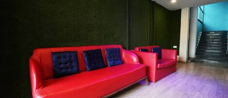 Un intérieur moderne avec un canapé en cuir rouge et un fauteuil assorti, un escalier et un mur texturé de couleur verte.