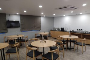 Un comedor moderno con mesas y sillas redondas, una encimera de cocina con electrodomésticos y un televisor montado.