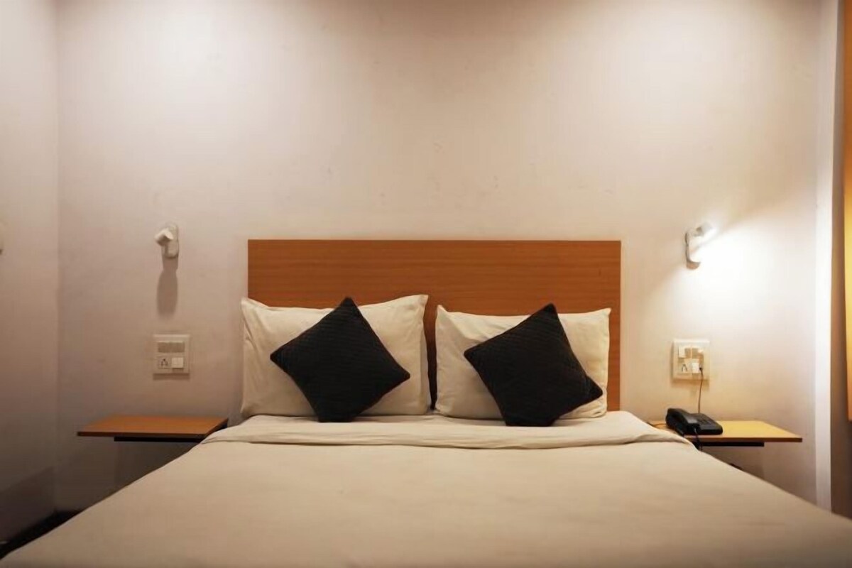 A hotel room with a wooden headboard, two black pillows, a white bedspread, and a bedside table with a phone.