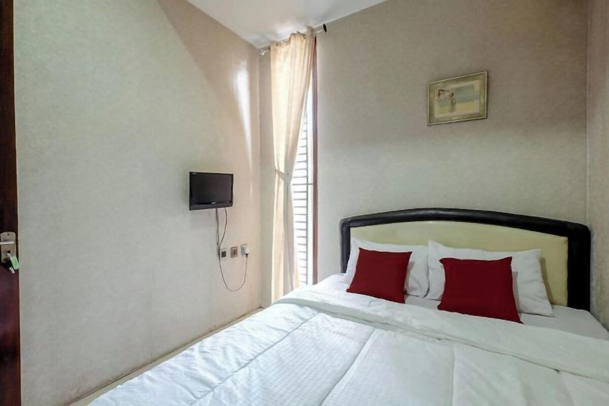 A hotel room with a bed, a television mounted on the wall, and a window with curtains.
