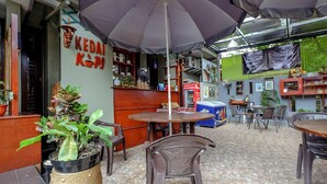 Un área de estar interior con mesas y sillas, un paraguas grande y un letrero que dice "KEDAI KOPI".