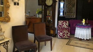 Una sala de estar con dos sillones, un reloj grande, una mesa con un florero y un sofá morado.