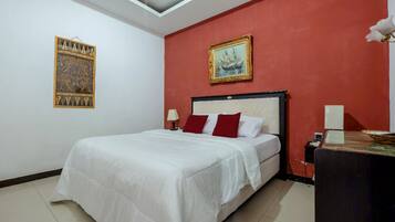A bedroom with a bed, a nightstand, a desk, a red wall, and two framed pictures.