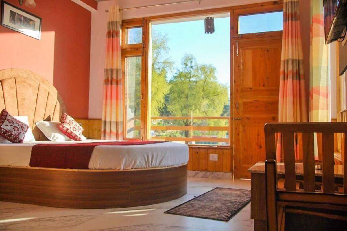 Une chambre avec un lit en bois, une fenêtre avec des rideaux et une vue sur les arbres à l’extérieur.