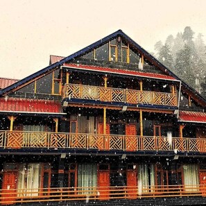 Una casa de madera de dos pisos con balcones y un techo inclinado, rodeada de nieve.