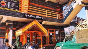 Un edificio con una cafetería llamada 'Cafe Saffron' y un letrero de 'Kesar Travels' que anuncia servicios como reservas de hotel y actividades de aventura.