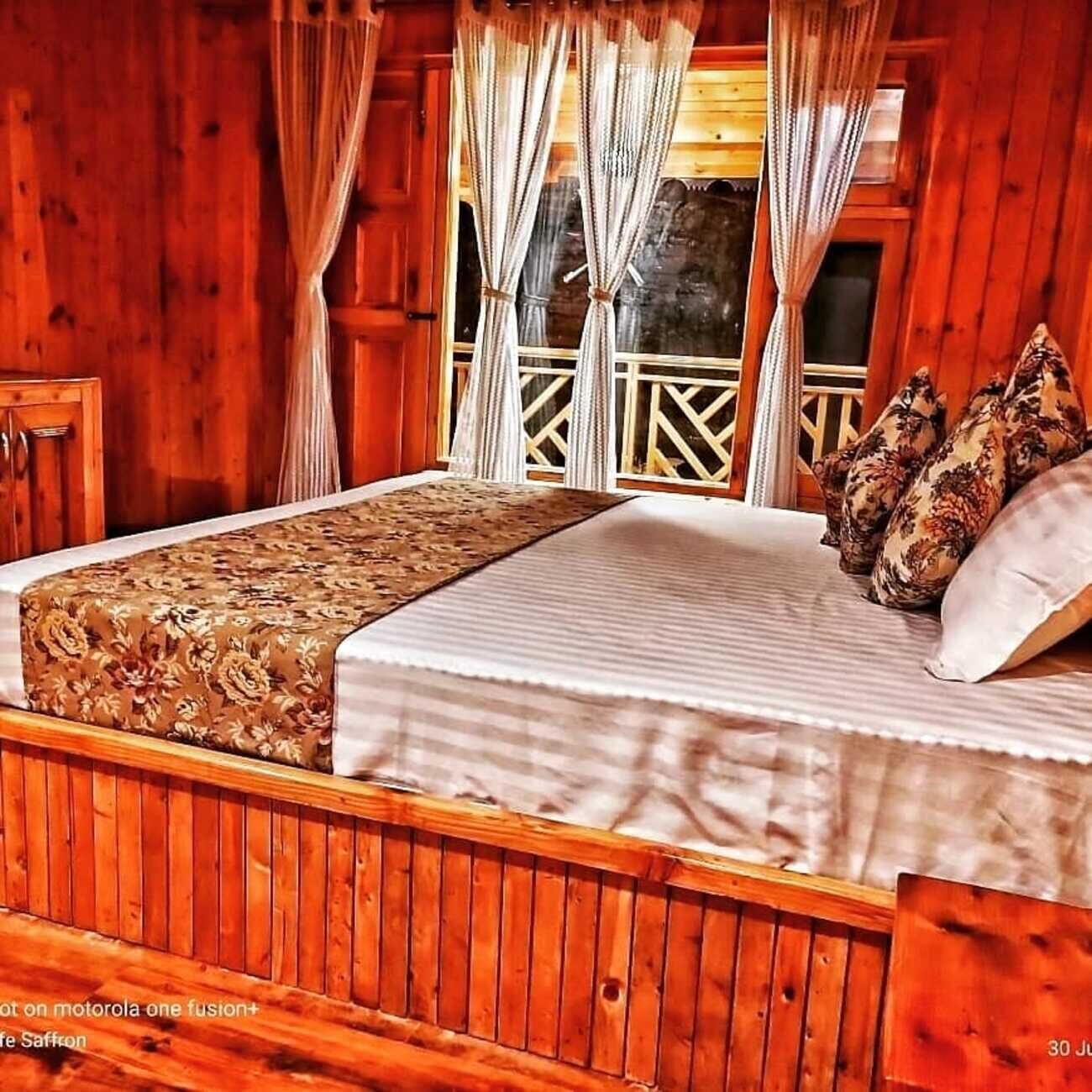 A wooden cabin bedroom with a bed, curtains, and a window with a view.