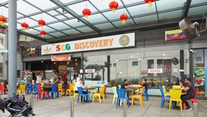 An outdoor dining area with colorful plastic chairs and tables, a large fan, and red lanterns hanging from the ceiling. - Sungold Inn (Kuala Lumpur)