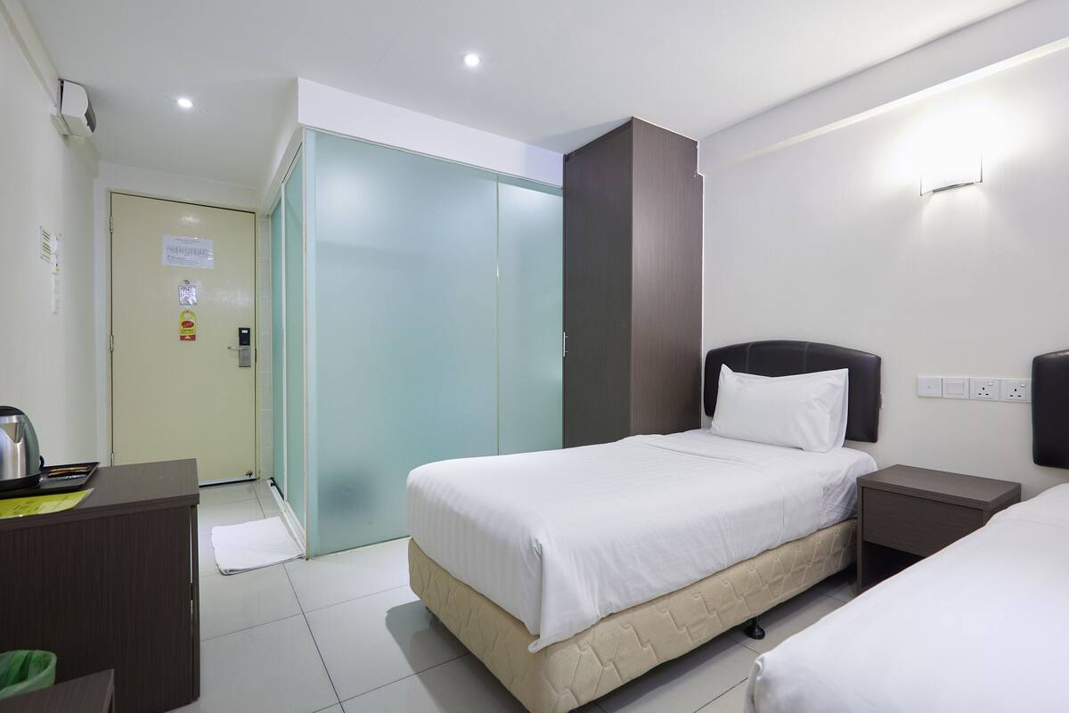 A hotel room with two beds, a desk, a wardrobe, and a bedside table.