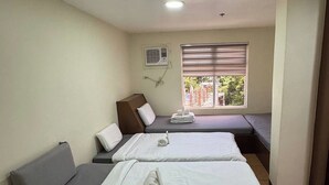 Habitación de hotel con dos camas, un sofá, una ventana con persianas, un equipo de aire acondicionado y una lámpara de techo.