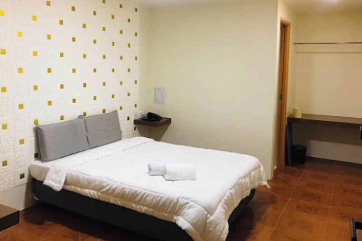A bedroom with a bed, pillows, a nightstand, and a wall with a geometric pattern.