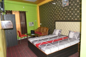 A hotel room with a large bed, a red chair, a small table, and a television. - Hotel Mountain View And Rooftop Restaurant (Pithoragarh)