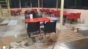 A covered outdoor dining area with red tables and chairs, a tiled floor, and a view of the night sky. - Hotel Mountain View And Rooftop Restaurant (Pithoragarh)