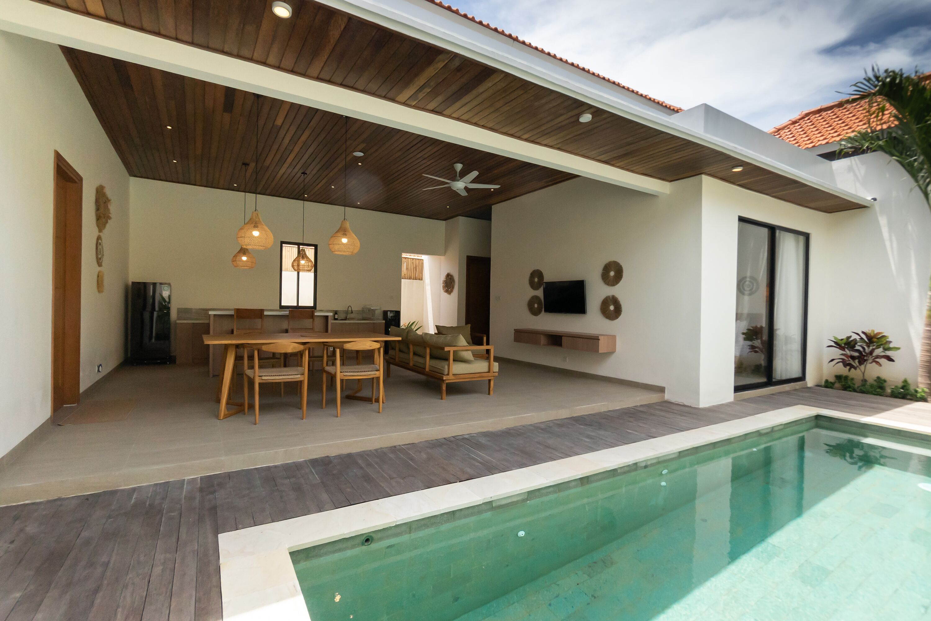 A modern outdoor living area with a pool, wooden furniture, and a ceiling fan.