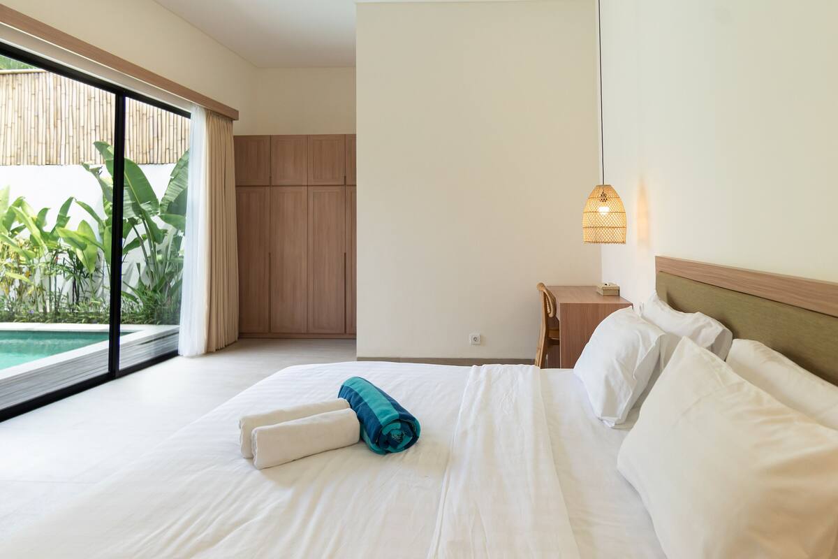 Quarto de hotel com uma cama grande, uma escrivaninha e vista para uma piscina.