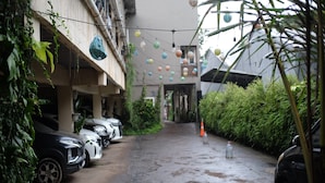 A narrow alley with parked cars, greenery, and string lights.