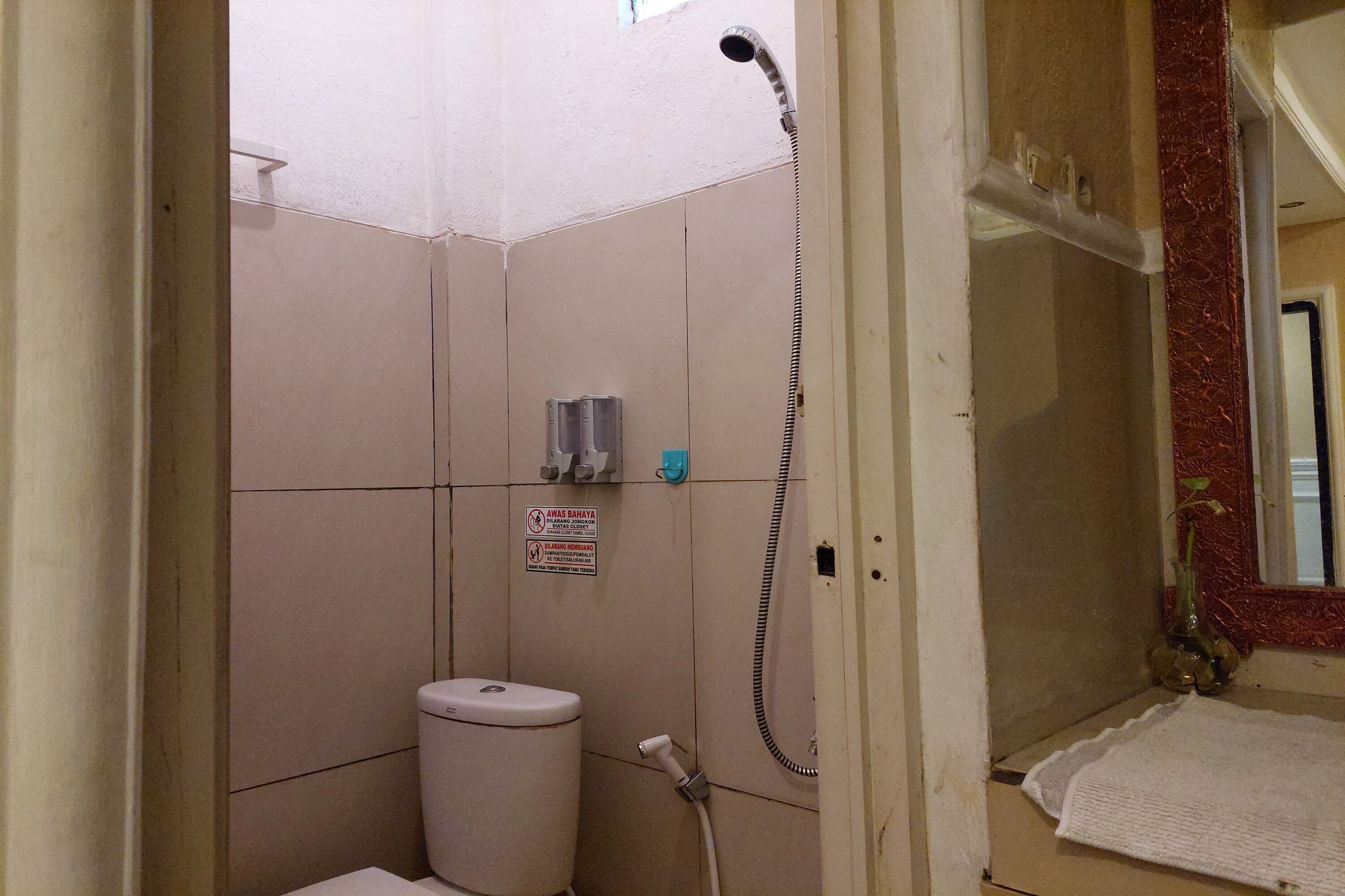 Une petite salle de bain carrelée, équipée de toilettes, d’une douche et d’un porte-serviettes.