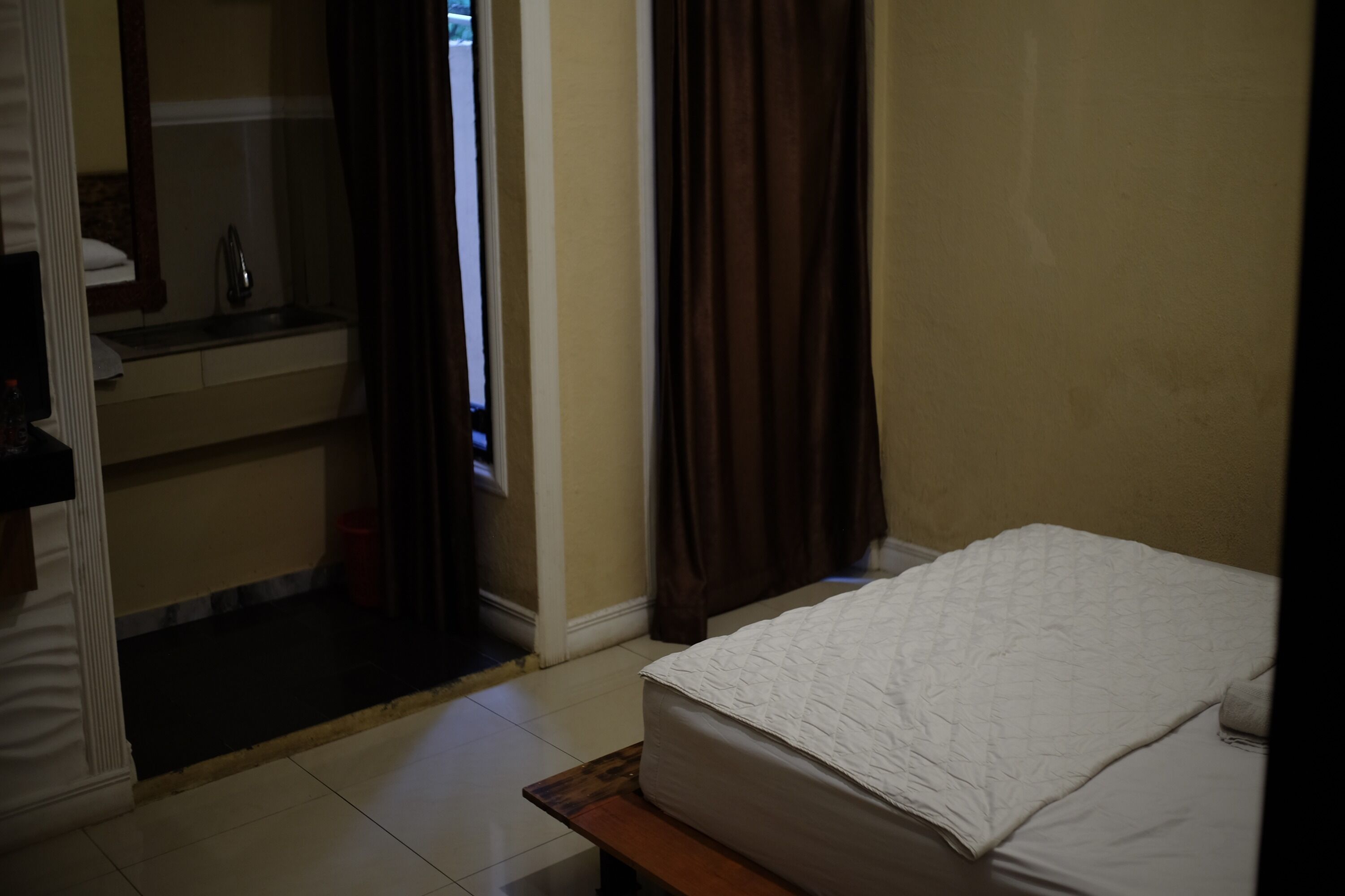 Een slaapkamer met een bed, een spiegel, een wastafel en een raam met gordijnen.