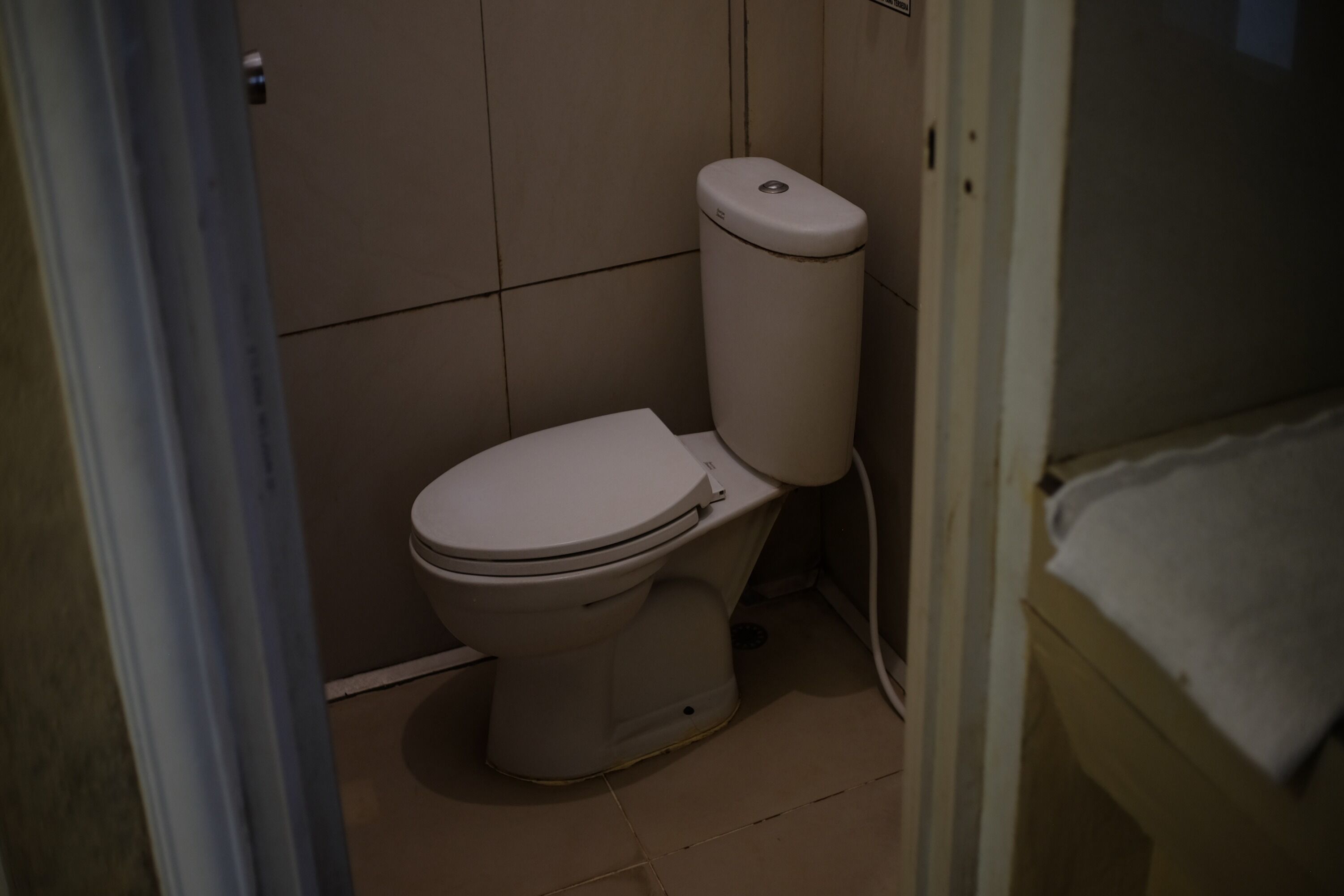 Eine Standardtoilette in einem Badezimmer mit gefliestem Boden und Wand.